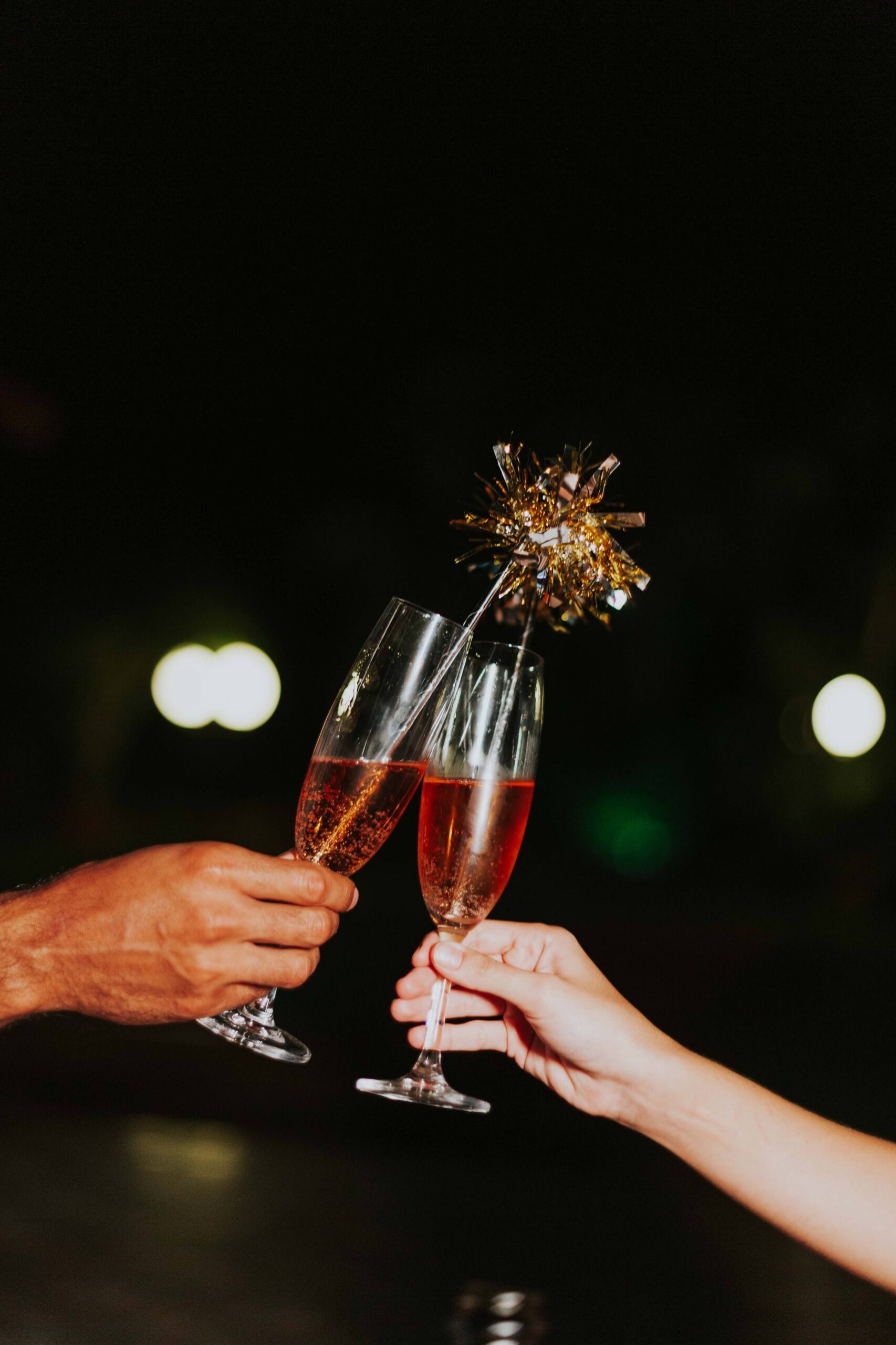Two hands clinking champagne glasses outdoors at night, perfect for festive occasions.