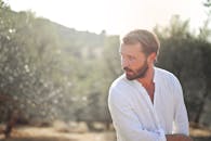 Portrait of a contemplative man in white shirt outdoors with a serene rural backdrop.